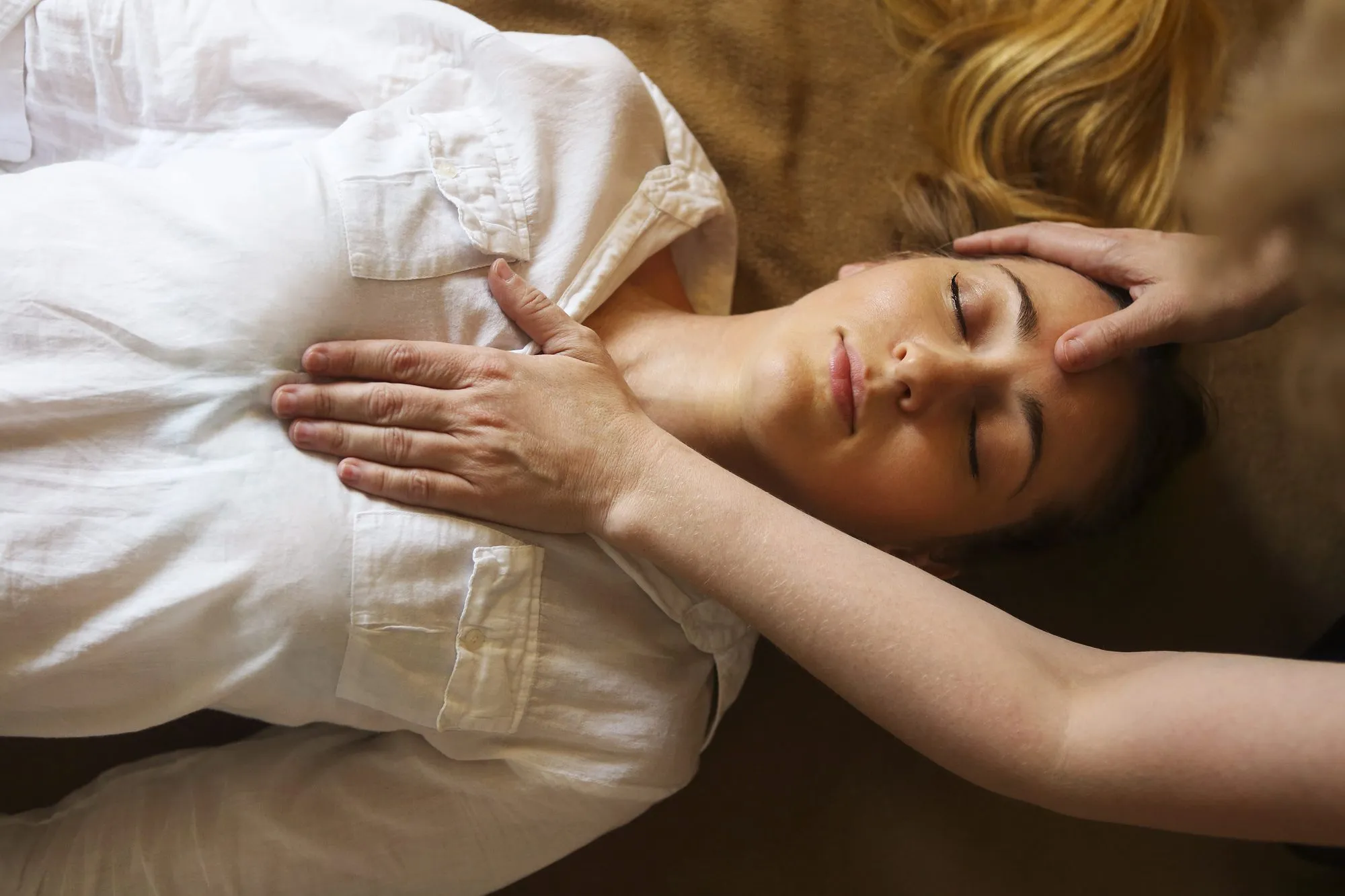 Femme allongée, yeux fermés, pendant qu'une praticienne pose les mains sur sa tête et son épaule